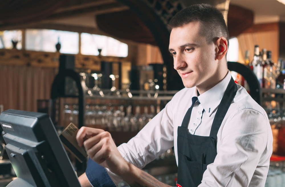 A waiter running a card through a touch-screen POS system at a bar
