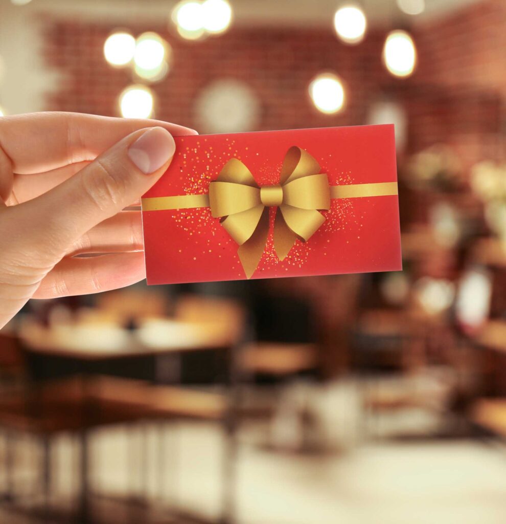 A hand holding a red giftcard with a gold bow