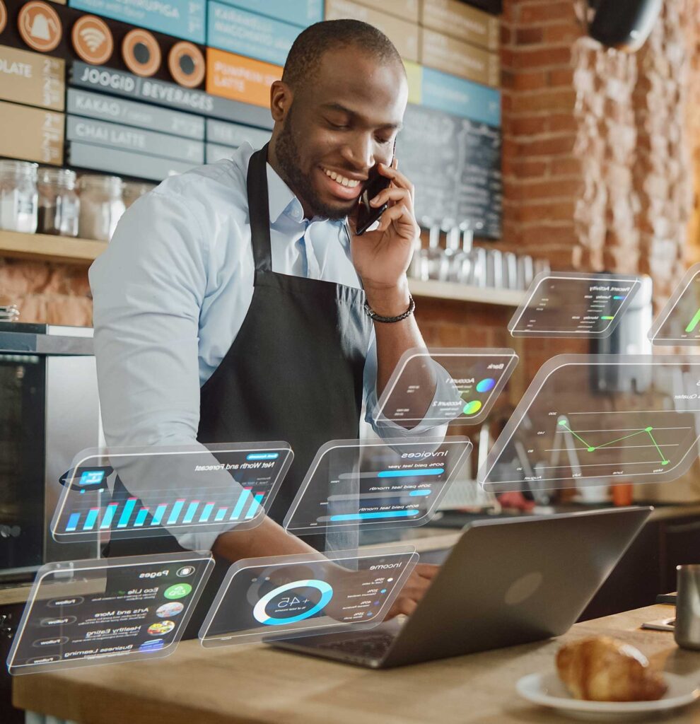 A man on a laptop at a store counter while talking on a cellphone