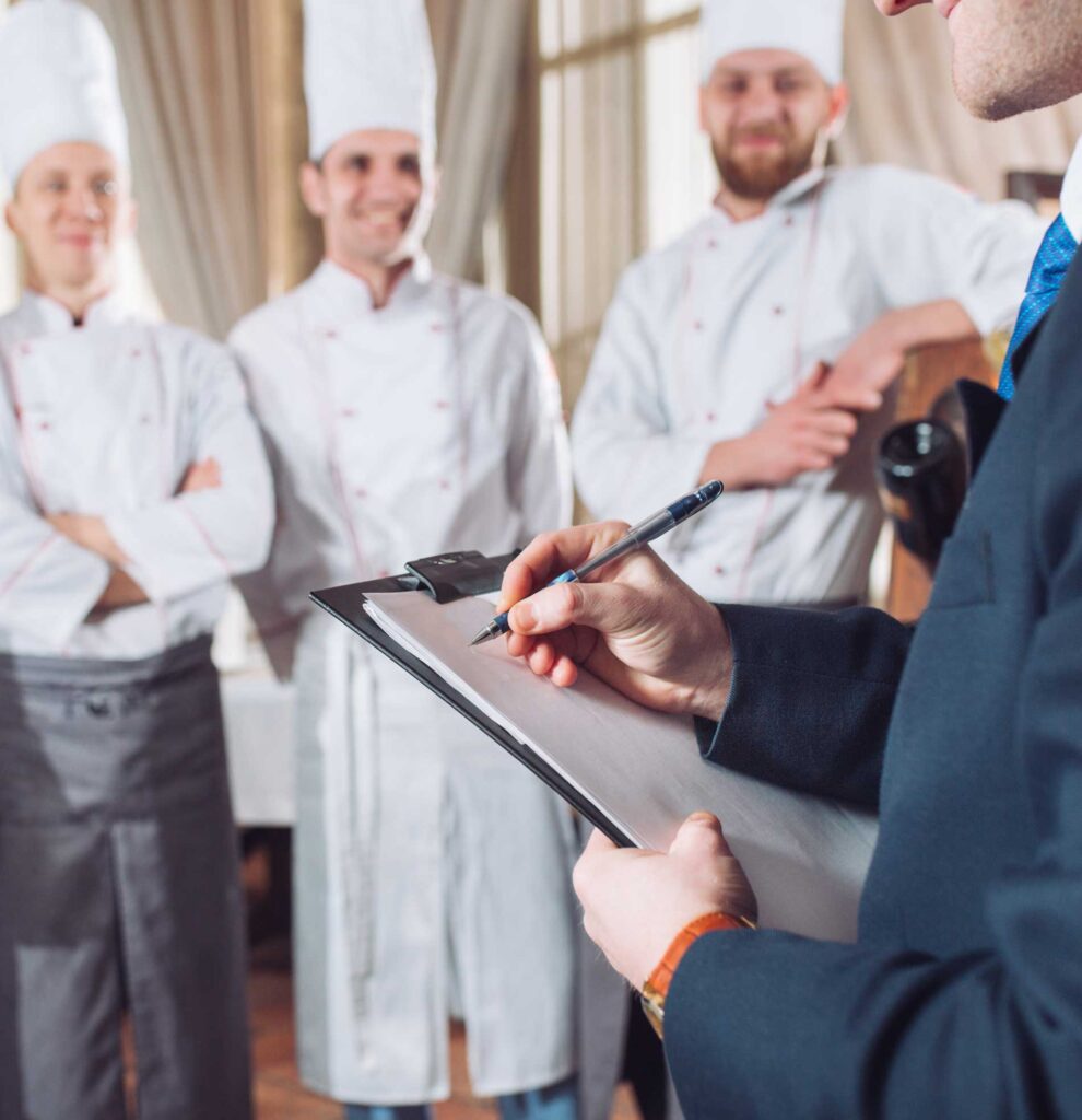 A man checking off a list while speaking to a group of chefs