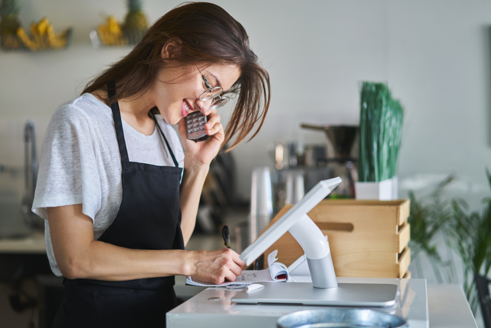 A barista on a phone and taking on order on a touchscreen POS system on the counter