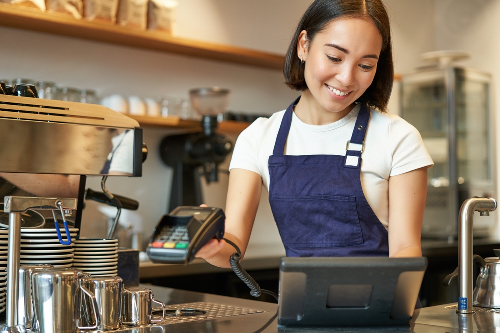 A young woman in a barista apron typing out an order on a touchscreen device